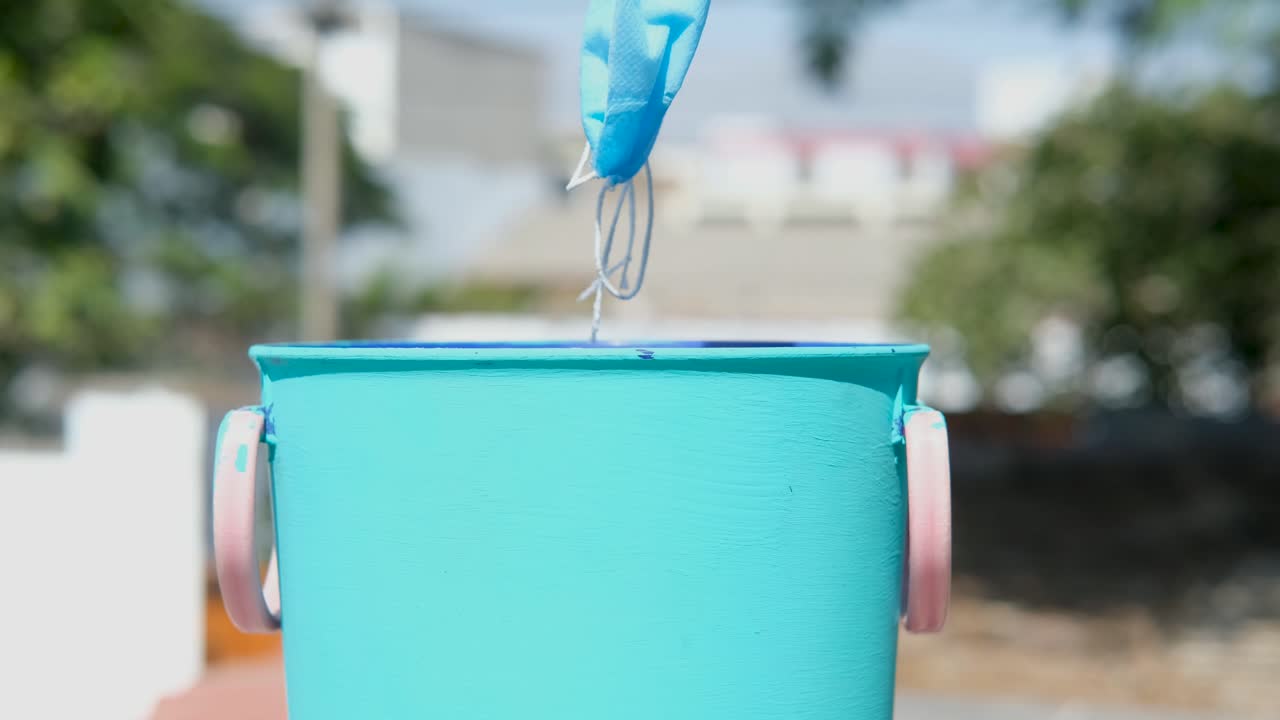 hand throws protective medical mask into the trash. day light, home.