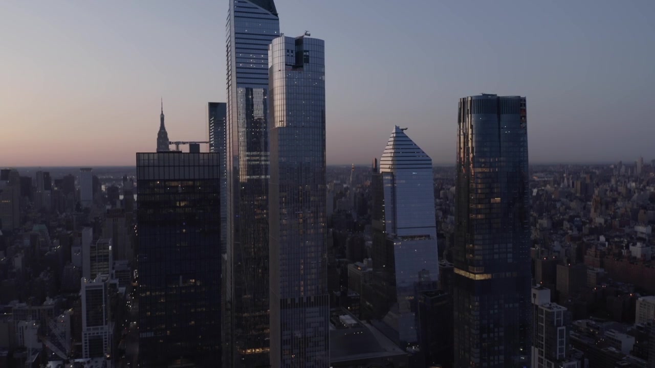I grattacieli di Hudson Yards si stagliano contro il cielo sfumato, morbido, blu-rosa e velato sopra Manhattan, ripresa aerea in ascesa con inclinazione verso il basso, sviluppo privato con bellissimi riflessi.