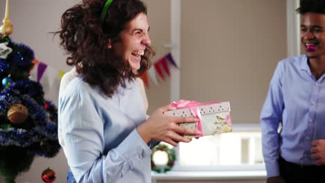 young attractive woman standing with her eyes closed by her female colleague while male workers surprising her and giving a