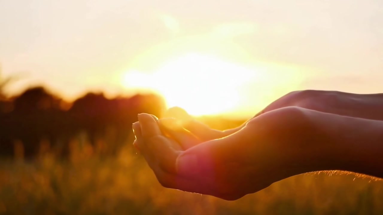 Persona con le mani tese verso un tramonto dorato