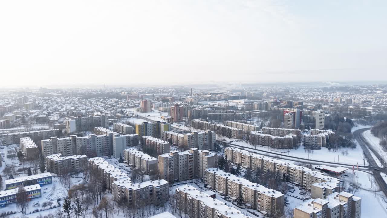 Drone video capturing a snow-blanketed urban landscape with residential buildings and roads. The wide angle showcases a serene city view from above, highlighting the winter season's beauty