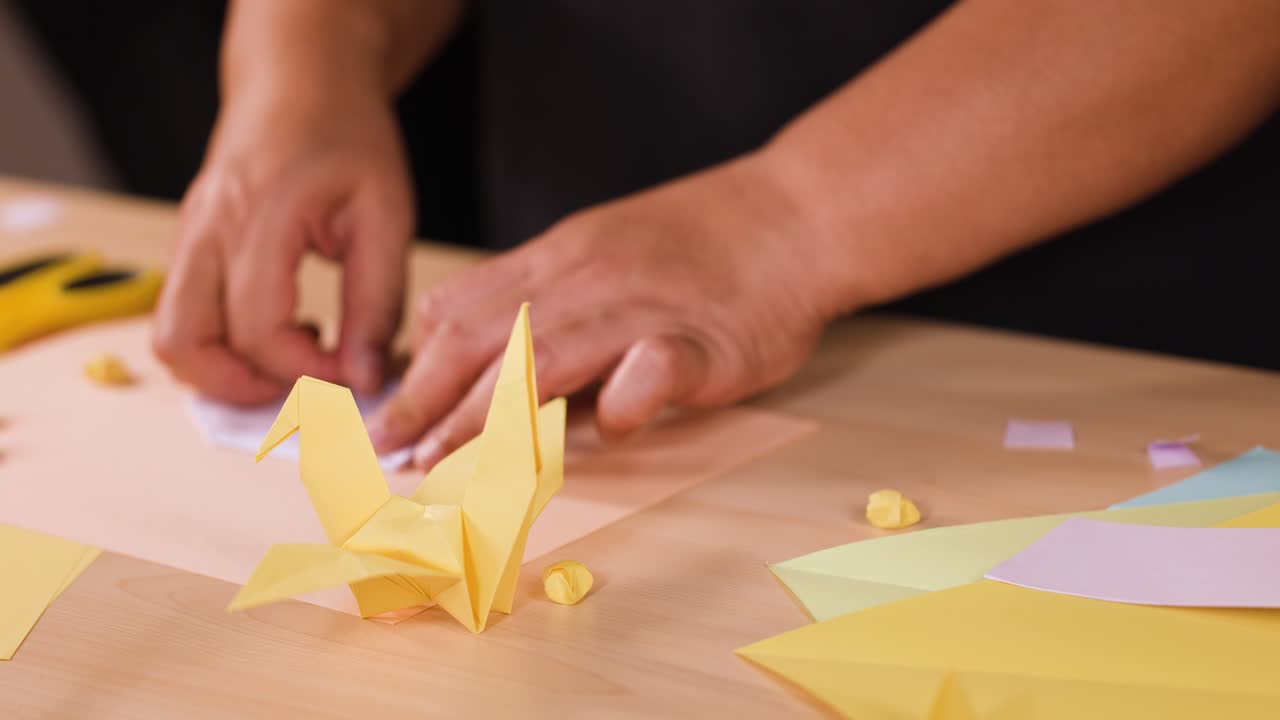 Primo piano di mani che piegano con cura la carta per creare una gru origami gialla
