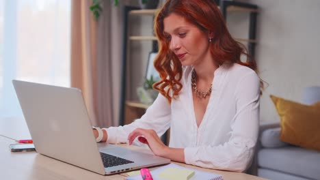 young cheerful woman correspondence with friends through laptop in home office