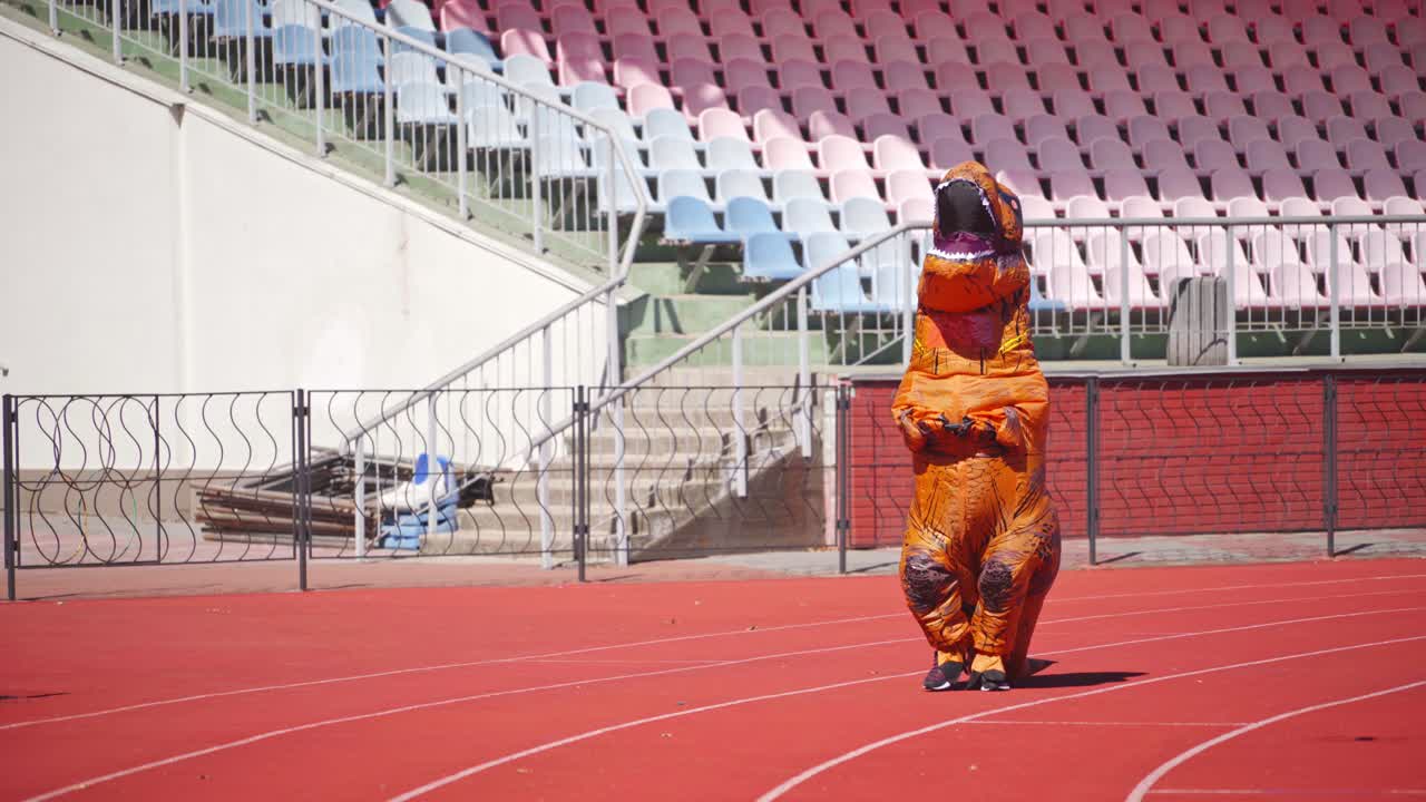 Big dragon in blow-up costume. Person dressed in funny orange costume walks on stadium in a sunny day.