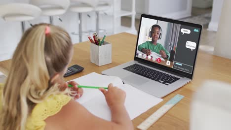 caucasian girl doing homework and having a video call with classmate on laptop at home