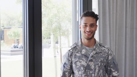 retrato de un feliz soldado masculino biracial en uniforme sonriendo en la sala de estar, espacio de copia, cámara lenta