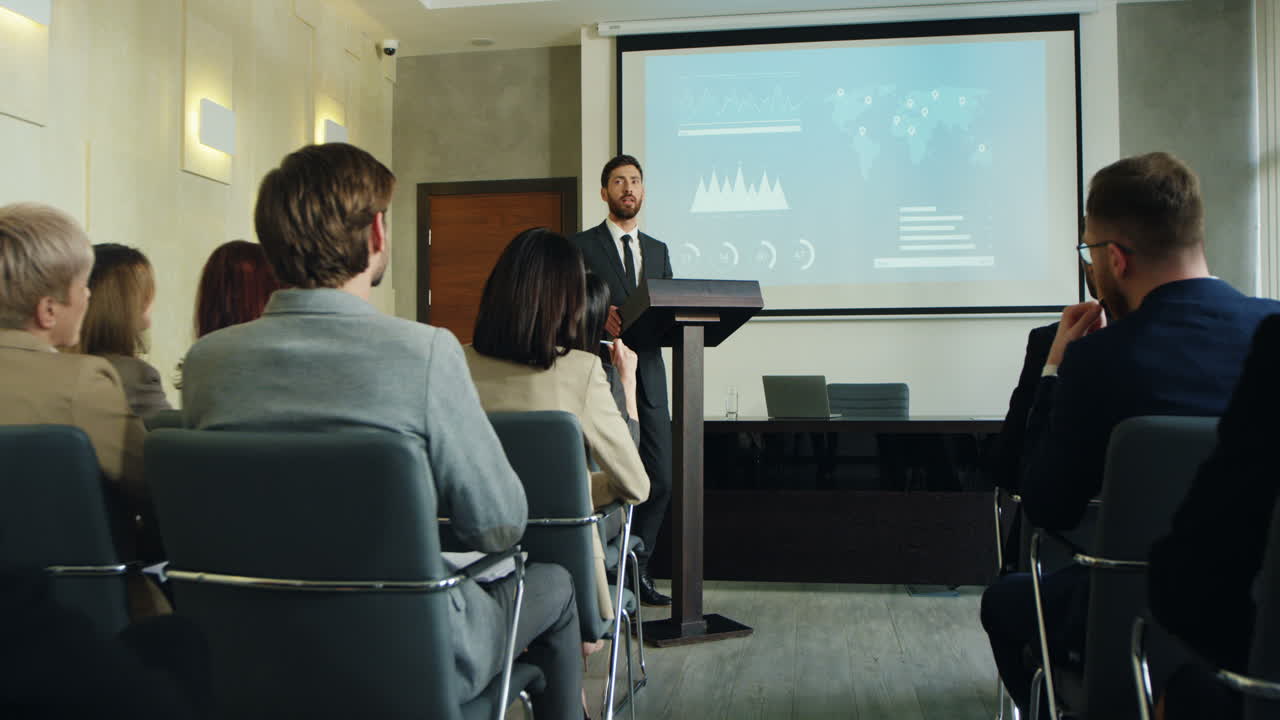 zoom de cámara sobre un hombre de negocios caucásico hablando en un podio en una sala de conferencias y mostrando algunos gráficos y gráficos en la pantalla grande