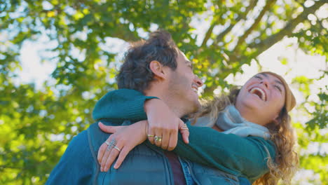 feliz pareja amorosa sonriendo como hombre dar mujer a cuestas en el parque de otoño