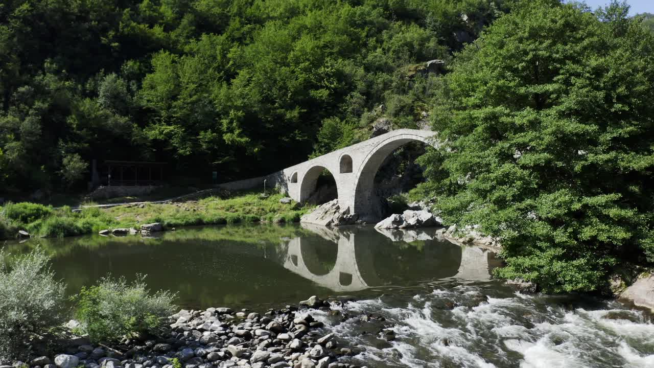 프레임의 왼쪽에 드론을 펴고 불가리아의 로도프 산맥에 있는 아르디노에 위치한 악마의 다리의 전체 면을 드러낸다.