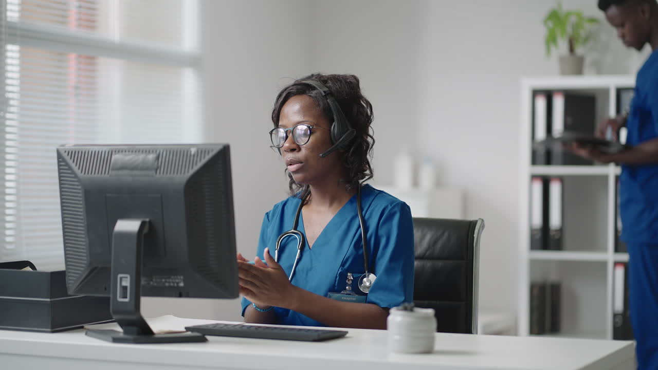 African Female medical assistant wears white coat headset video calling distant patient on computer. Doctor talking to client using virtual chat computer app. Telemedicine remote healthcare