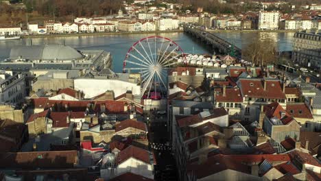 Drohne-Fliegt-über-Dächer-Des-Stadtzentrums-Von-Bayonne-Mit-Riesenrad-Und-Fluss-Im-Hintergrund,-Frankreich