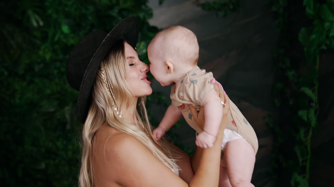 Happy smiling mother wearing black hat holds her cute baby. Woman waves her child and kid smiles happily.