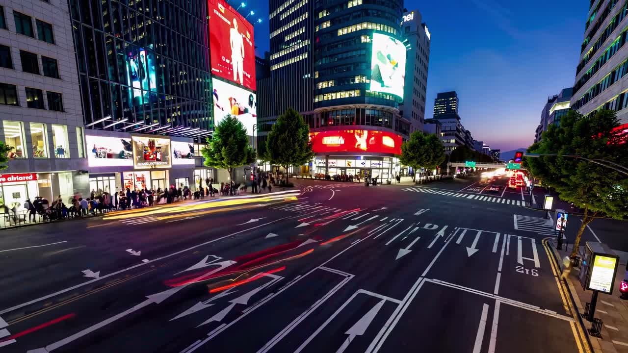 Colorful city lights illuminate busy streets during dusk with vibrant advertisements and moving traffic in a lively urban setting