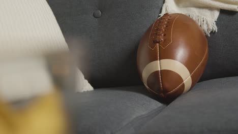 lounge at home of person watching american football game on tv with snacks and ball