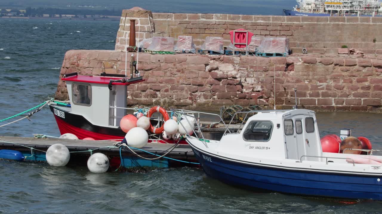 Two small fishing boats bob at dock in bright daylight, mild camera movement, coastal harbor