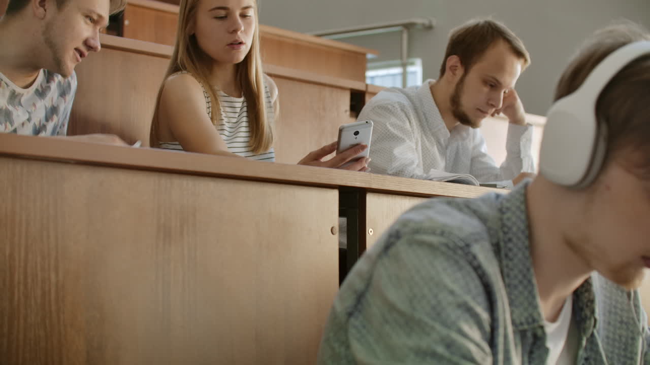 chicas bonitas estudiantes están usando teléfonos inteligentes viendo pantalla hablando y riendo sentadas en escritorios en la universidad. redes sociales internet millennials y concepto de educación