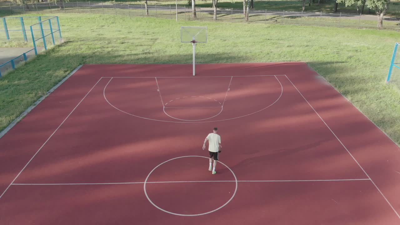 drone capturando a un hombre anotando un tiro de baloncesto perfecto desde arriba, destacando su habilidad y determinación, capturando el momento del triunfo durante el día en américa