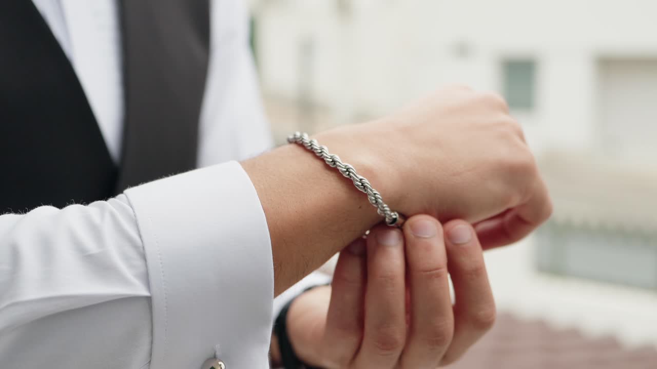 close up of man wearing elegant silver bracelet while dressing in formal white shirt and vest