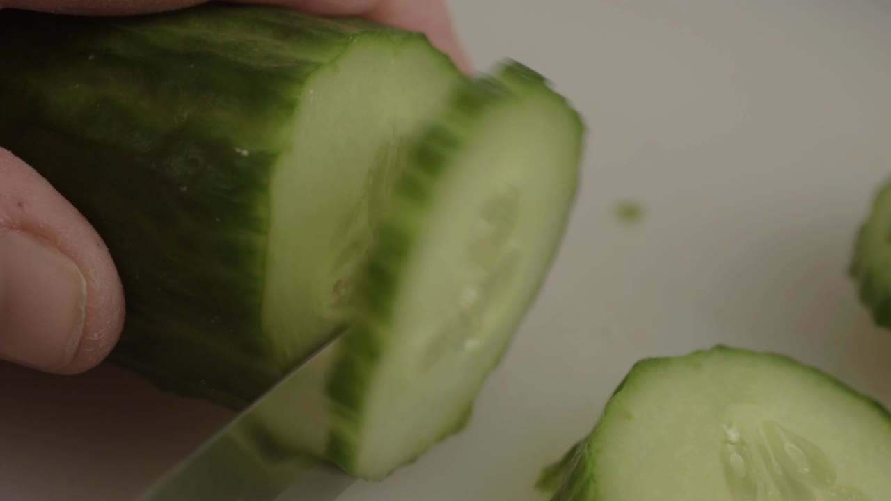Hand slicing a cucumber with knife detailed macro shot