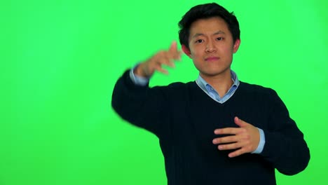 젊은 아시아인 남자가 카메라에 접근하기 위해 몸짓을 한다 - 그린 스크린 스튜디오