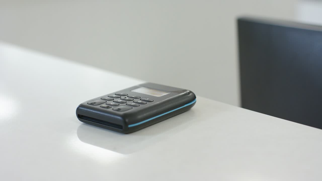 Camera is dollying in, highlighting black keypad device sitting on white desk and reflections