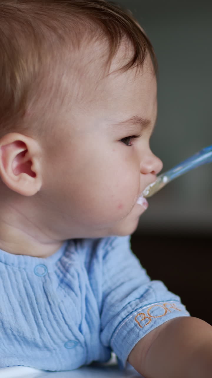 Lovely kid eating dairy sitting at the feeding table. Beautiful child nutrition from spoon. Close up. Vertical video
