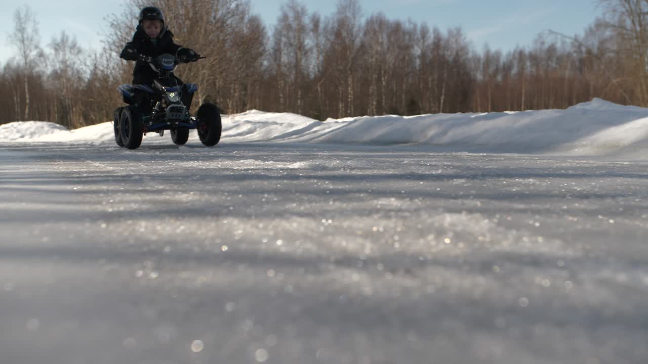 Giovane ragazzo caucasico guida un quad su strada ghiacciata, ripresa in movimento dal basso