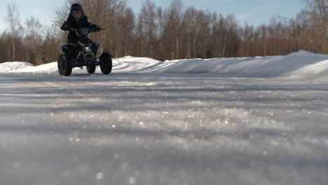 young caucasian boy rides atv on icy road, low tracking shot