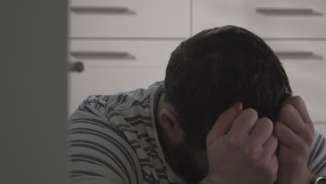 young stressed man with heartache sits on floor covering face with hands, close dolly shot