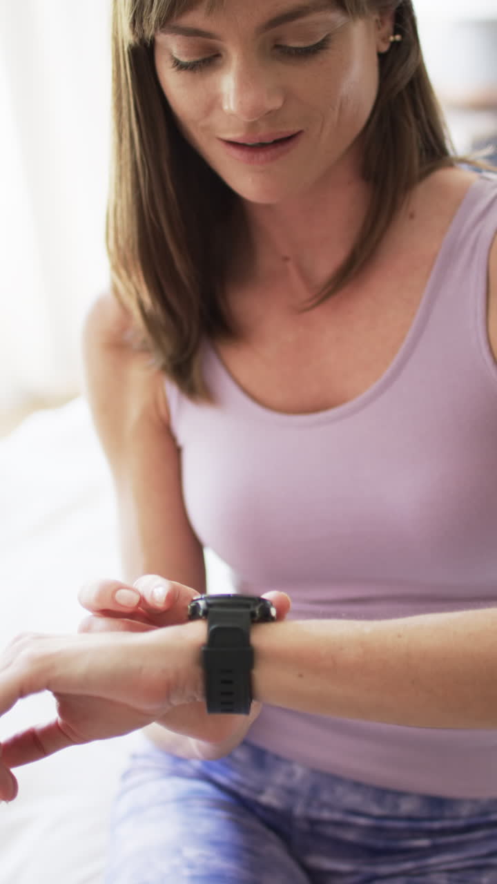 Vertical video: Caucasian woman checking smartwatch at home, light background