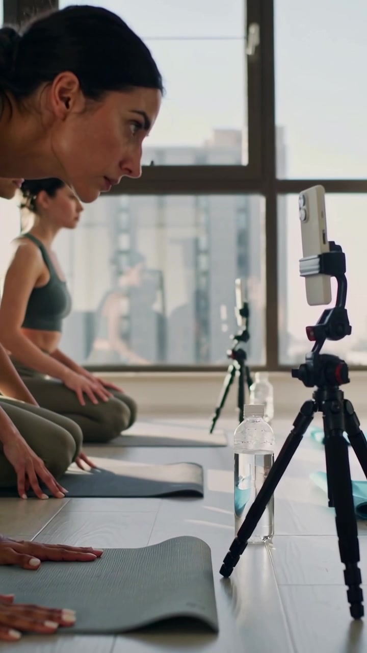 Vertical video: Phone tripod pinging women in tops kneeling on mats in studio taking bottle, rising
