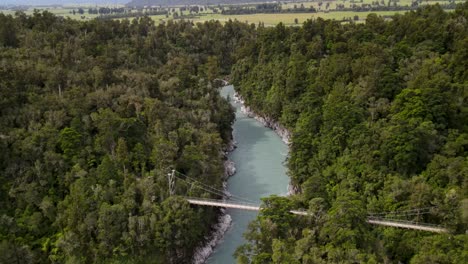 Turquoise-and-green-water-in-Hokitika-Gorge-surrounded-by-lush-native-forest---aerial-reveal-of-suspension-bridge-and-New-Zealand-landscape