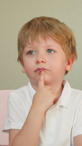 preschooler raises hand answering teacher question. diligent small boy touches chin listening to educational information carefully. pupil in class