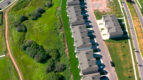 Rapid-development-suburban-townhomes-sprawl-across-open-green-land-in-bozeman-montana,-traffic-circles-on-roads,-aerial-panoramic-overview