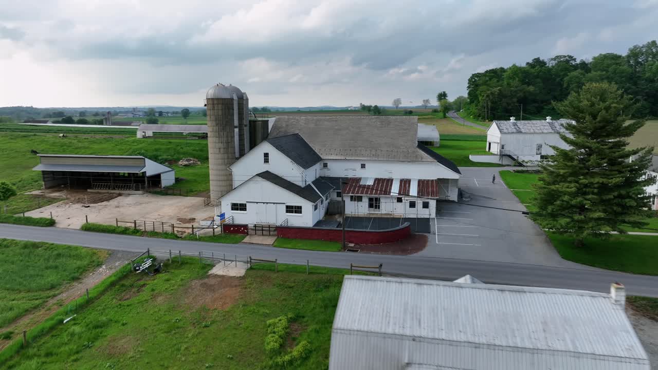 Cars on rural street of american countryside. Drone flight around farmstead with barn, stable and silo storage. Cloudy day in Spring season. Amish farm in Pennsylvania, United states.