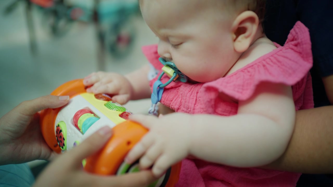 Bebê menina segurando um brinquedo interativo com assistência, explorando e aprendendo enquanto um dos pais a apoia