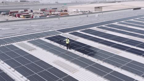 hombre con chaleco reflectante y casco de seguridad limpiando paneles solares en la parte superior de un gran almacén industrial en dubai, emiratos árabes unidos