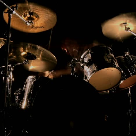 a drummer plays on a darkened stage