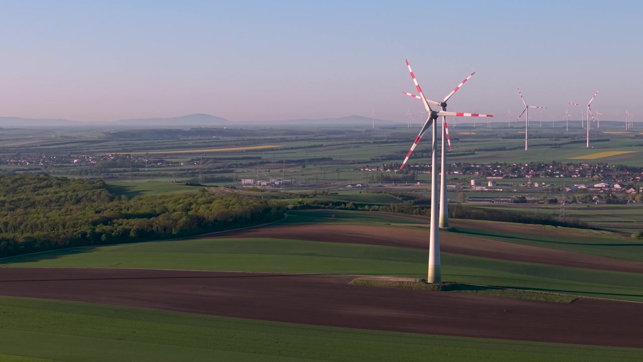 Vista aerea di una turbina eolica nella luce nebbiosa del mattino su un paesaggio agricolo. Singolo mulino a vento bianco che si erge sopra campi nebbiosi e terreni agricoli a mosaico. Energia rinnovabile in atmosfera rurale.