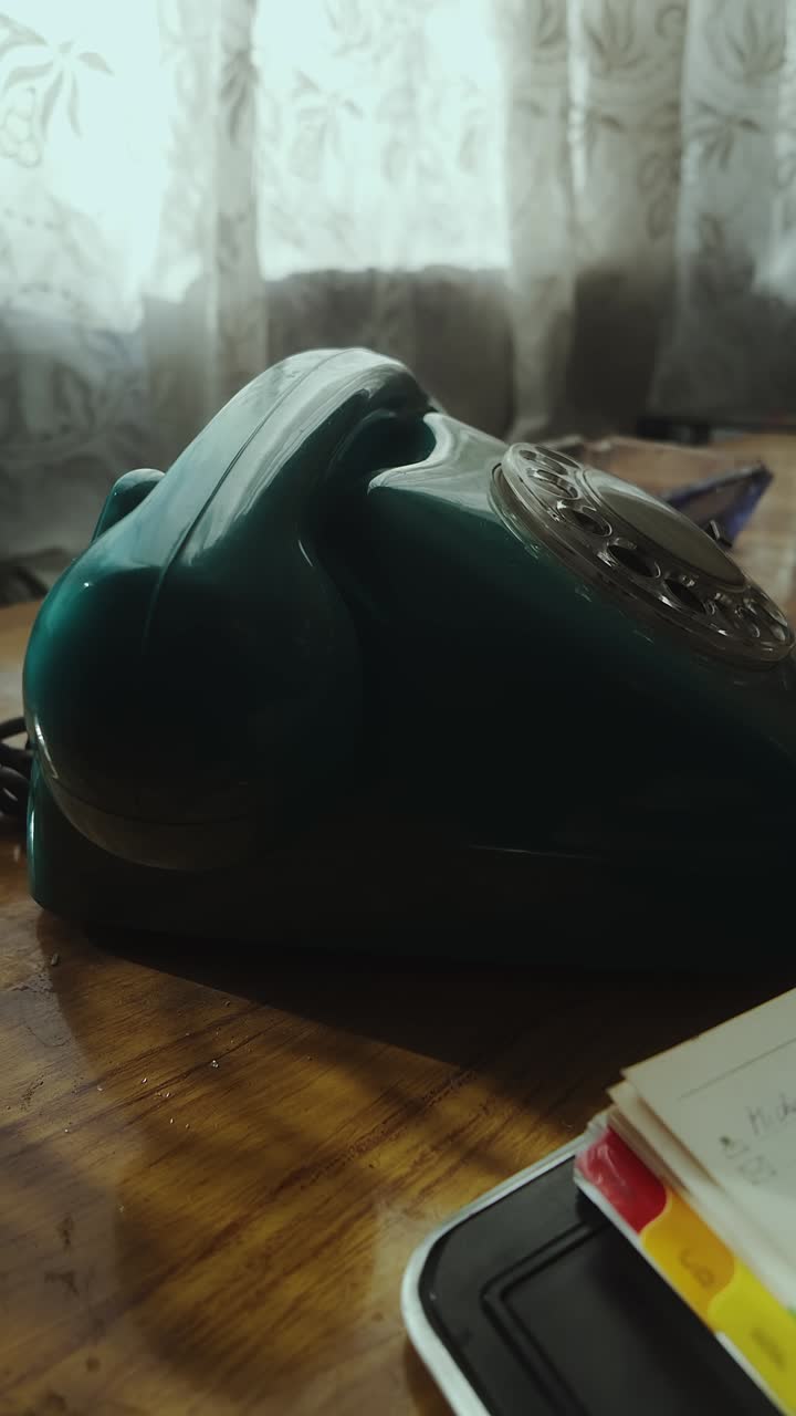 Person dials contact number on retro telephone by desk window VERTICAL