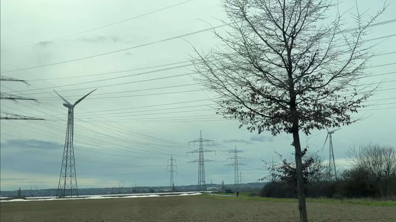 Power line with many straw poles and wind turbines next to it in the evening sky