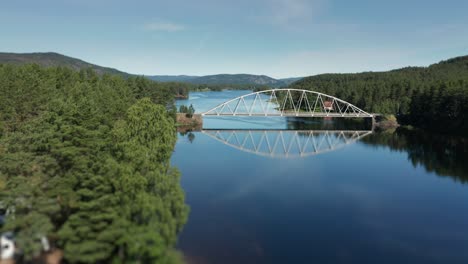 a spectacular flight over otra river: a camping, where minivans are parked under the pines, and boats are lying on the sand, sharp reflections of the trees and of a bridge seen on still water surface