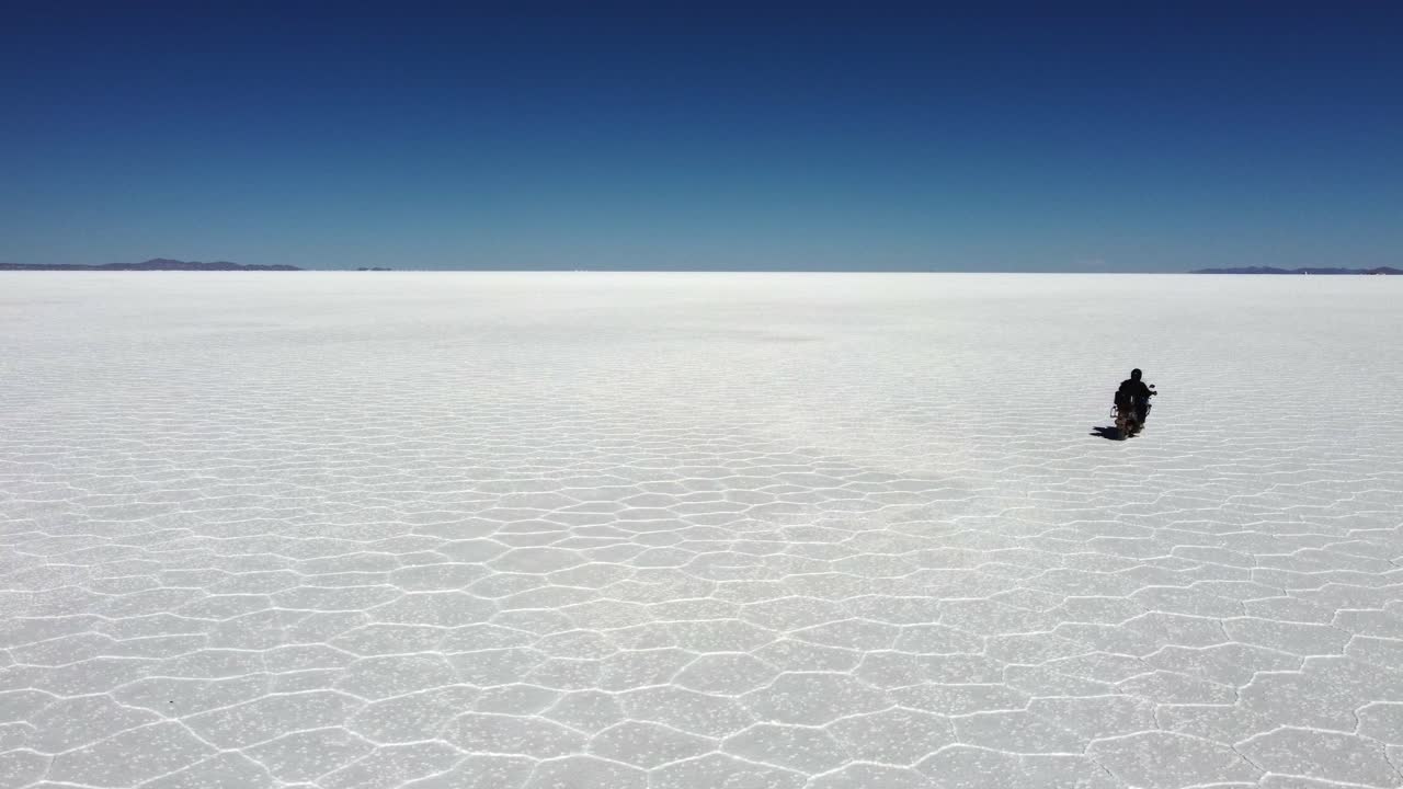Pengendara Sepeda Motor Melaju Menuju Cakrawala Datar yang Jauh di Salar de Uyuni, Bolivia