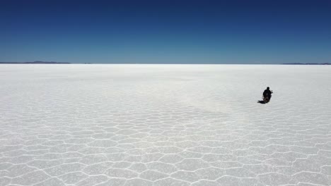 motorcyclist rides toward distant flat horizon on uyuni salt, bolivia