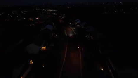 Dark-aerial-shot-of-car-driving-in-American-neighborhood-at-night