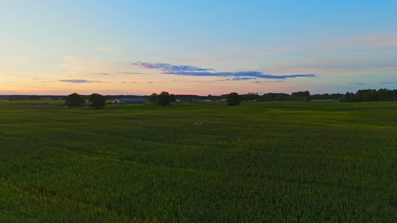 Agro drone flying low over the crop fields of Latvia during post sunset blue light hour. Slow aerial reverse tracking shot