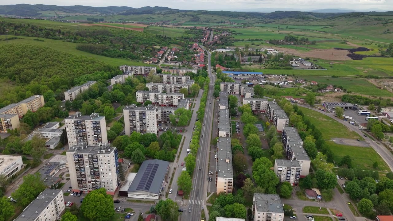 Ilmakuva dronella esikaupunkialueesta, jossa on asuinkerrostaloja vihreiden puiden ja maaseutumaiseman ympäröimänä.