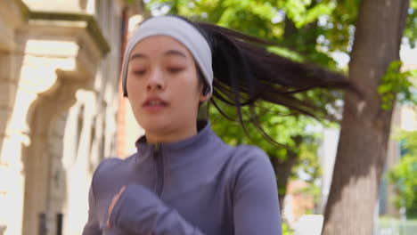 Close-Up-Front-View-Of-Young-Woman-Exercising-Running-Along-City-Street-Wearing-Wireless-Earbuds-Stopping-To-Rest