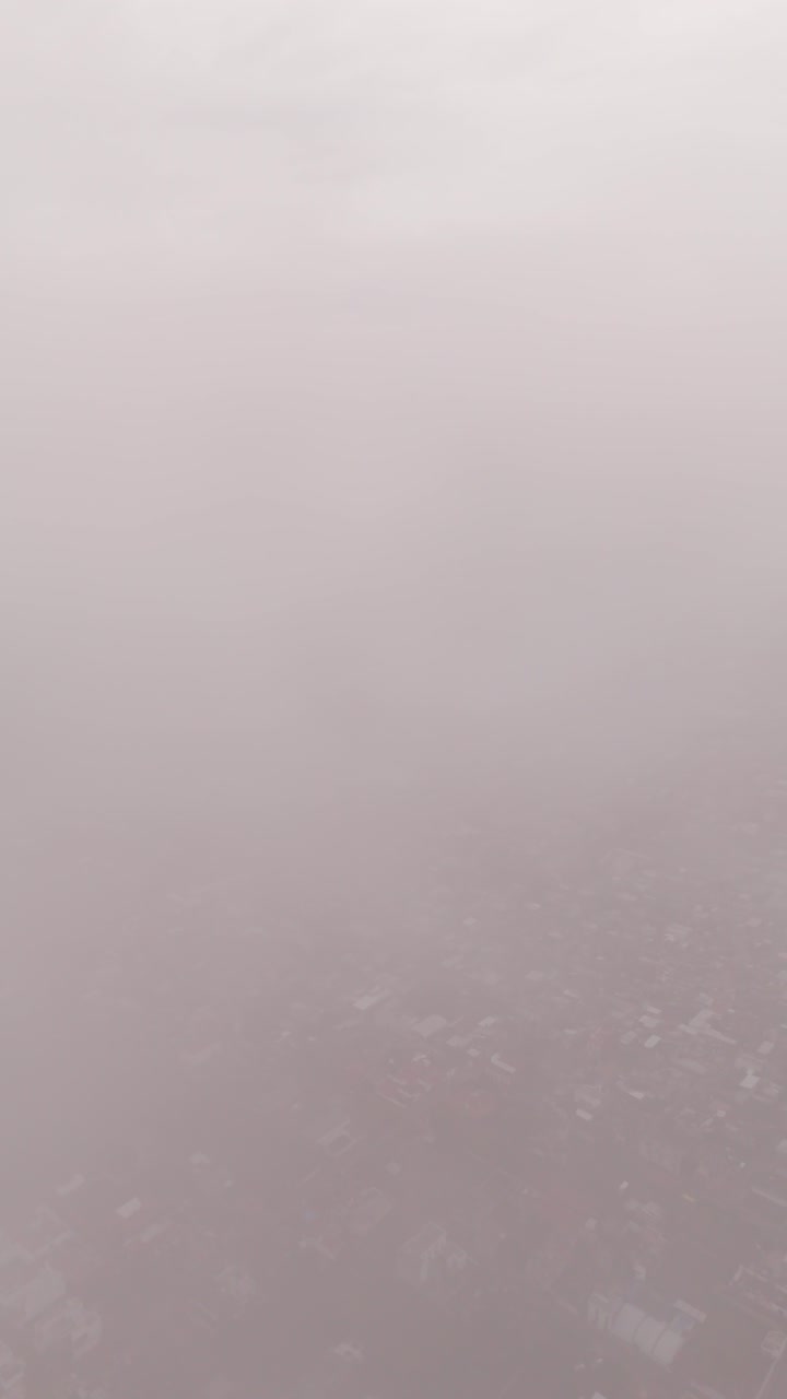 Drone ascends through clouds, revealing a cityscape filled with red-roofed houses and buildings.