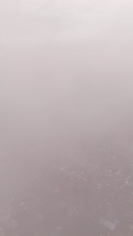 drone ascends through clouds, revealing a cityscape filled with red-roofed houses and buildings.